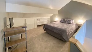 A bedroom with a sloped ceiling, a bed with patterned pillows, a desk with a chair, and built-in shelving. - Cozy Condo in the Heart of Smugglers' Notch Resort (Cambridge)