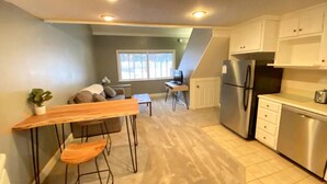 A compact kitchen with a refrigerator, a dining table with chairs, and a window providing natural light. - Cozy Condo in the Heart of Smugglers' Notch Resort (Cambridge)