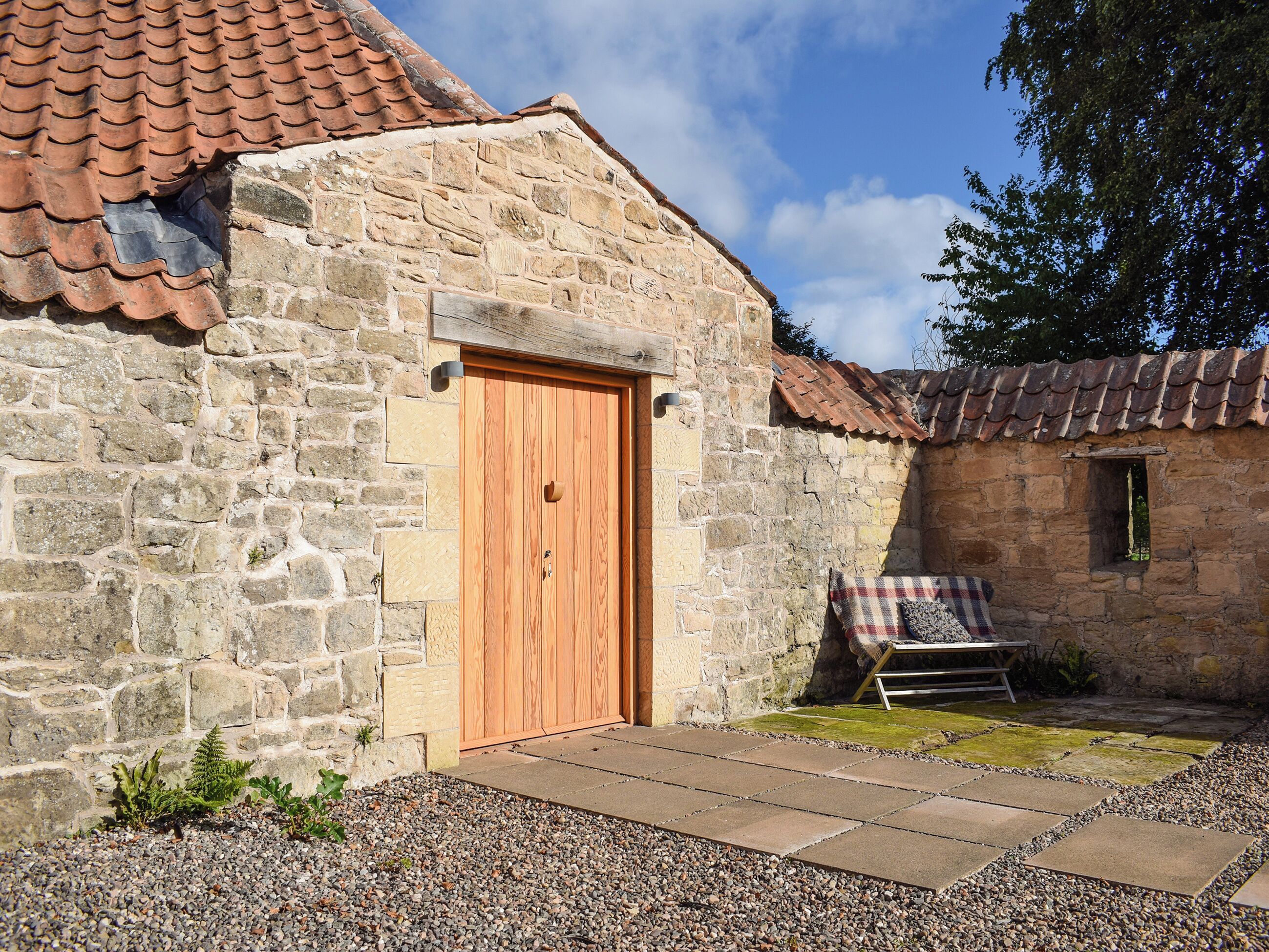 A stone building with a wooden door, a small window, and a bench with a plaid blanket.