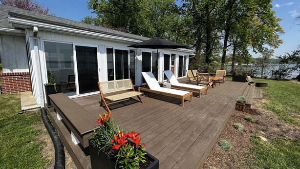A covered deck with lounge chairs and a table, surrounded by a grassy area and a body of water. - Upper Chesapeake Getaway - Newly Renovated (Perryville)