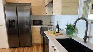A modern kitchen with stainless steel appliances, wooden cabinets, a black sink, and a window providing natural light. - Upper Chesapeake Getaway - Newly Renovated (Perryville)