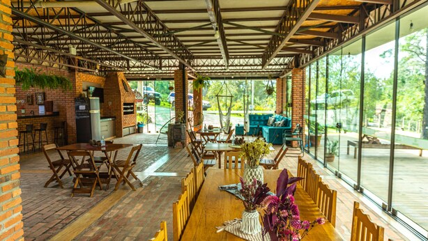 Un área de comedor al aire libre techada, con paredes de ladrillo, mesas y sillas de madera.