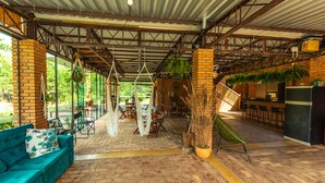Un espacio interior amplio con suelo de ladrillo, un sofá verde, plantas colgantes y una zona de bar.