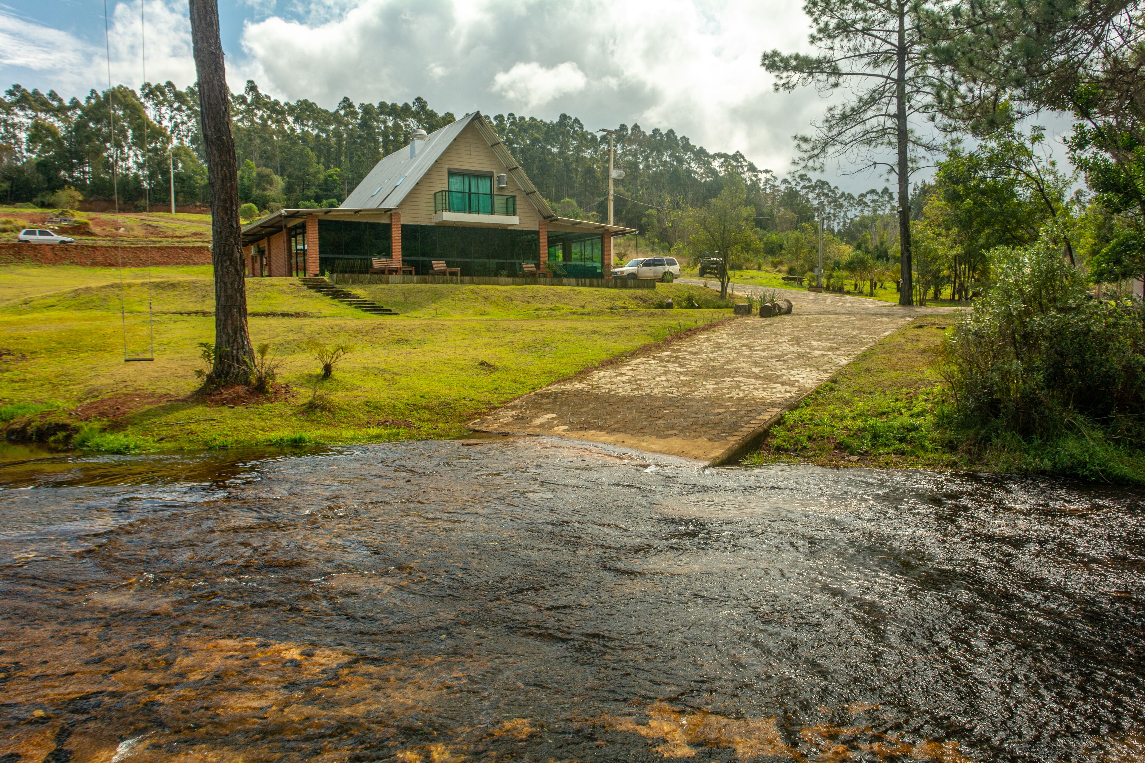 A house with a sloped roof, a covered porch, and a small stream in front.