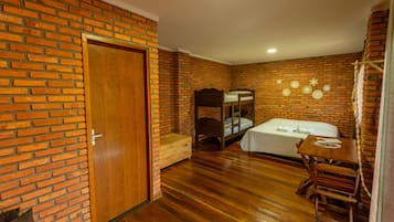 Una habitación con pared de ladrillo, puerta de madera, literas, una mesa pequeña con sillas y un banco de madera.