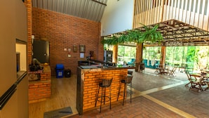 Un espacio interior amplio con pared de ladrillo, una barra con taburetes y una zona de estar cubierta con mesas y sillas.