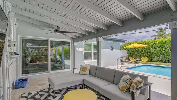 Un espace extérieur abrité avec des sièges, une piscine, un ventilateur de plafond et une table jaune.