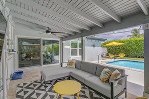Ein überdachter Außenbereich mit Pool, Deckenventilator und einem gelben Tisch.