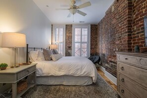 A bedroom with a bed, bedside lamps, a dresser, a radiator, and a brick wall.