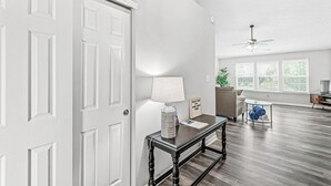 A spacious living room with a wooden floor, a white door, a ceiling fan, and a large window with blinds. - 3-min from downtown Fishers (Fishers)