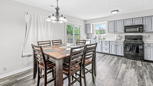 A modern kitchen with white cabinets, a black stove, and a dining area with a wooden table and chairs. - 3-min from downtown Fishers (Fishers)