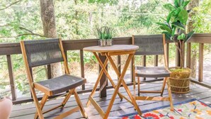 A wooden deck with two chairs and a small table, surrounded by trees and greenery. - The Boho Loft: colorful, cozy, comfortable 1BR (Hot Springs)