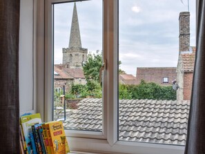 A window with a view of a church spire and residential buildings.