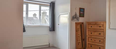 Une chambre à coucher comprenant un lit, une commode, un radiateur, une fenêtre et un luminaire suspendu.