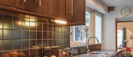 A kitchen with dark wooden cabinets, a tiled backsplash, a stainless steel sink, and a fruit basket on the counter.