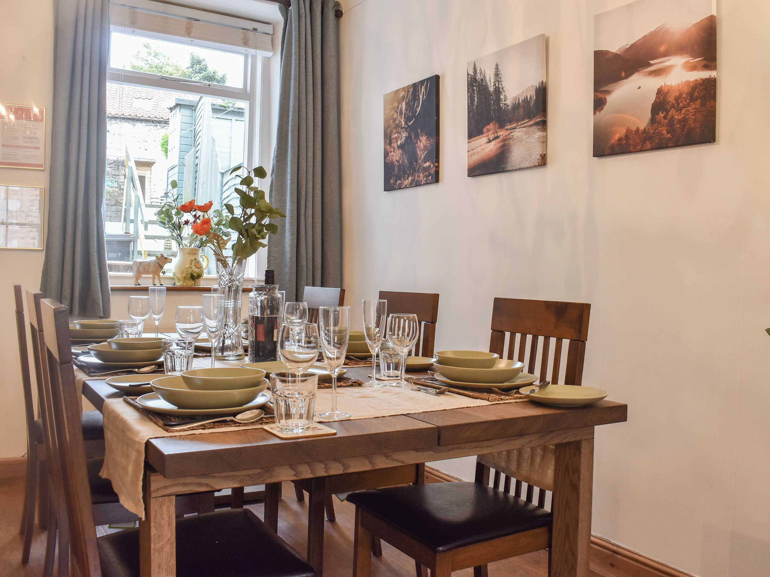 A dining table set with plates, glasses, and cutlery, surrounded by wooden chairs.