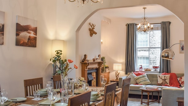 Un coin repas avec une table dressée pour six personnes, une cheminée et un espace salon confortable avec un canapé et une table d’appoint.