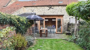 Un bâtiment en pierre avec un toit en tuiles, une porte en bois et une terrasse avec des chaises et une table.