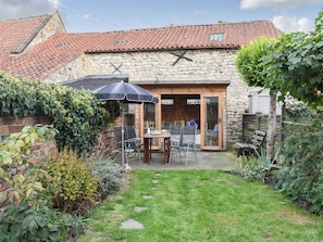 A stone building with a tiled roof, a wooden door, and a patio with chairs and a table. - 3 bedroom accommodation in Pickering (Pickering)