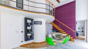 A modern interior with a glass dining table, green chairs, a purple accent wall, and a spiral staircase. - Design Duplex at National Museum (Napoli)