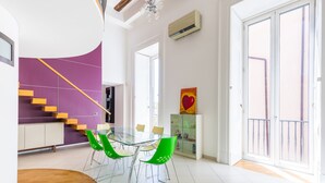 A modern dining area with a glass table and green chairs, a purple accent wall, a staircase, and a balcony with a railing. - Design Duplex at National Museum (Napoli)