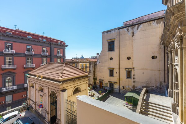 Une cour intérieure agrémentée d’une petite fontaine, entourée d’immeubles dotés de balcons et de fenêtres en arc de cercle.