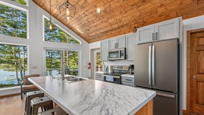 A modern kitchen with a large marble island, stainless steel appliances, and a wooden ceiling.
