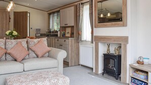 A cozy living room with a sofa, ottoman, and fireplace. There is a kitchen area with cabinets and a stove. - 2 bedroom accommodation in Landford, near New Forest (Landford, near New Forest)