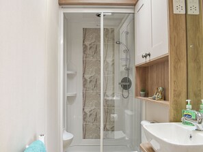 Une salle de bain moderne avec une douche à parois de verre, un lavabo blanc et des étagères en bois où sont rangés les produits de toilette.