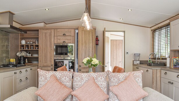 A modern kitchen with wooden cabinets, a built-in oven, and a dining area with a patterned sofa and decorative pillows. - 2 bedroom accommodation in Landford, near New Forest (Landford, near New Forest)