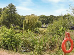 A serene garden with a pond, lush greenery, and a small building in the background.