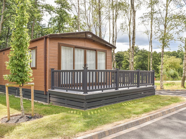 Une cabane en bois dotée d’un balcon, entourée d’arbres et bordée d’une zone herbeuse.