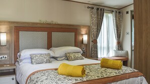 A hotel room with a large bed, a nightstand, a wooden headboard, and a window with curtains. - 2 bedroom accommodation in Landford, near New Forest (Landford, near New Forest)