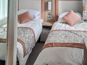 Une chambre d’hôtel avec deux lits, chacun agrémenté d’une couvre-lit à motifs et d’un élément décoratif marron. Une table de chevet se trouve entre les deux lits, avec une lampe et une prise électrique.