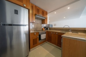 A modern kitchen with stainless steel appliances, wooden cabinets, a built-in oven, and a granite countertop. - Wayak 301 - Center of Playa del Carmen (Playa del Carmen)