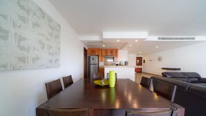 Zona pranzo con tavolo e sedie in legno, cucina sullo sfondo e un divano in pelle nera.