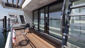 Ein moderner Bootsdeck mit Holzboden, Glastüren und einem Metallgeländer.