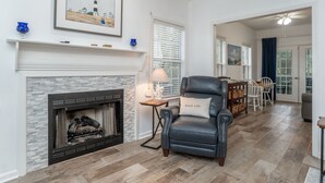 A living room with a fireplace, a leather chair, a dining area with a table and chairs, and a hallway leading to another room.