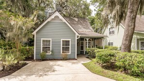 A single-story house with a front porch, surrounded by mature trees and well-maintained landscaping.
