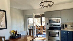 Een moderne keuken met roestvrijstalen apparatuur, een eethoek met een houten tafel en stoelen, en een kroonluchter.