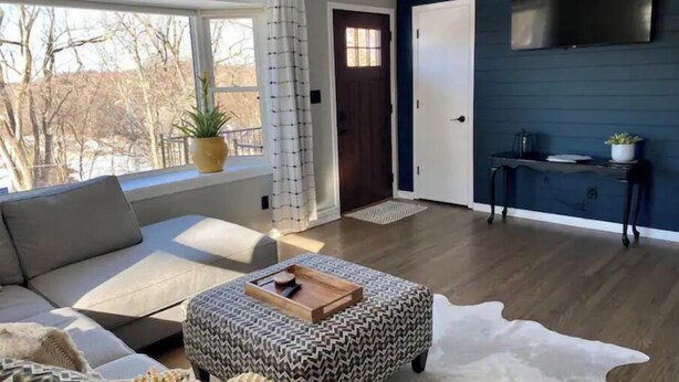 Een moderne woonkamer met een bank, poef en een flatscreen televisie aan de muur.