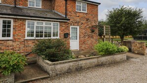 A two-story brick house with white-framed windows, a front door, and a small garden area with gravel and plants. - 2 Crosslands (York)
