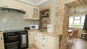 A kitchen with a stove, oven, microwave, and a stone wall. There is a window with a view of greenery. - 2 Crosslands (York)