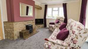 A living room with a stone fireplace, a sofa with floral upholstery, a television, and a window with curtains. - 2 Crosslands (York)