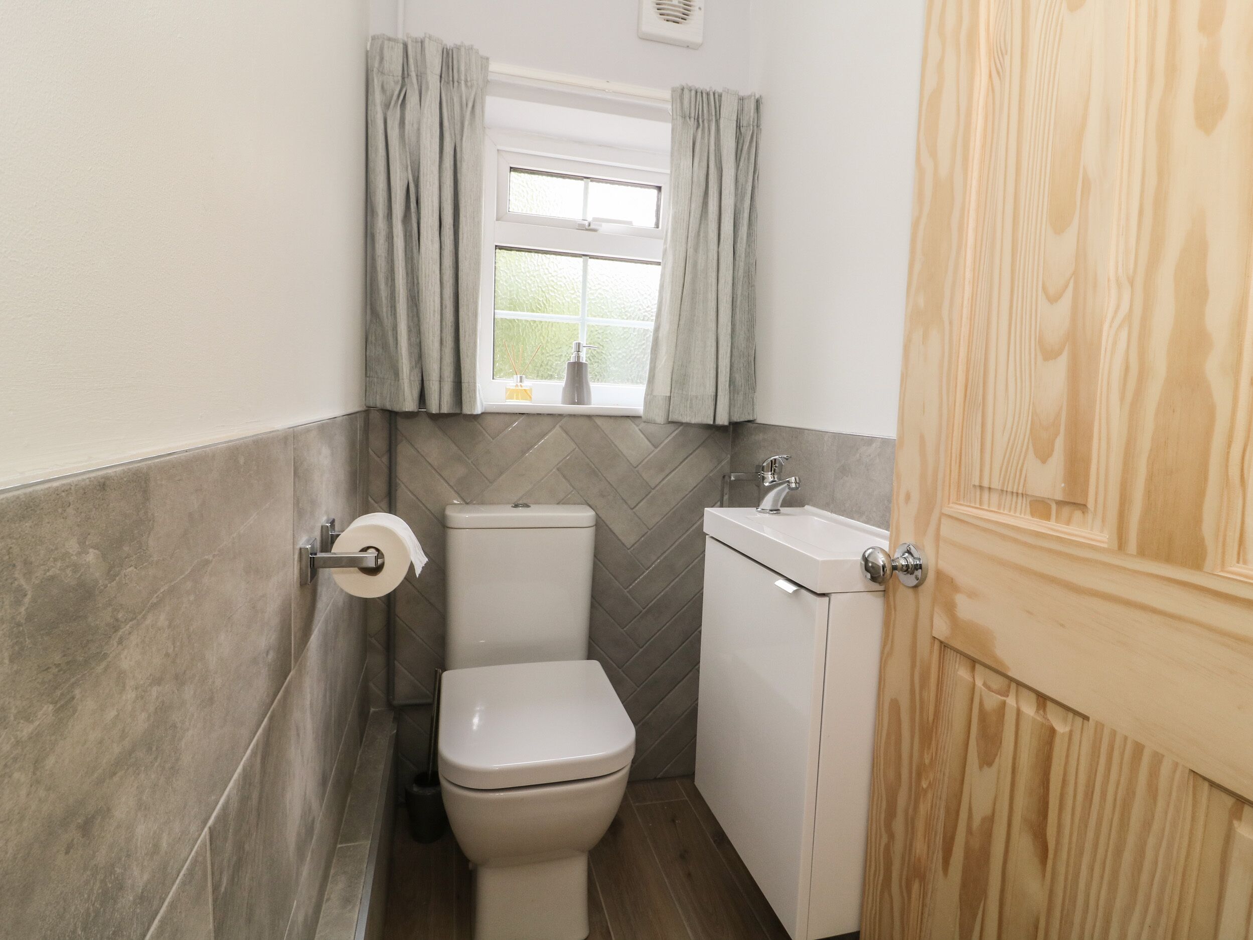 A compact bathroom with a toilet, sink, and window with curtains.