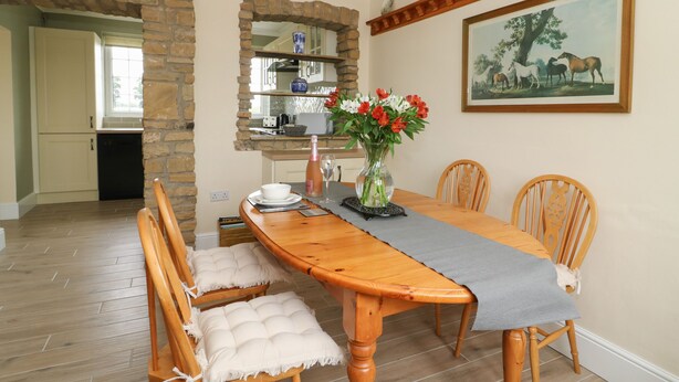 A dining area with a wooden table, cushioned chairs, a vase with flowers, and a painting on the wall. - 2 Crosslands (York)