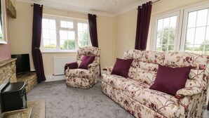 A living room with a floral sofa, a matching armchair, and a television on a stone fireplace. - 2 Crosslands (York)