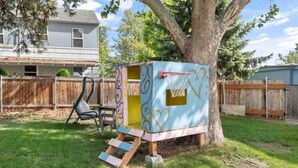 Une cabane de jeu avec une échelle et un portique à balançoire dans un jardin.