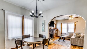 Un comedor con una mesa redonda y sillas, una araña y una chimenea al fondo.