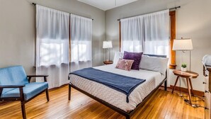 Un dormitorio con una cama, una silla, un ventilador de techo y dos mesitas de noche con lámparas.